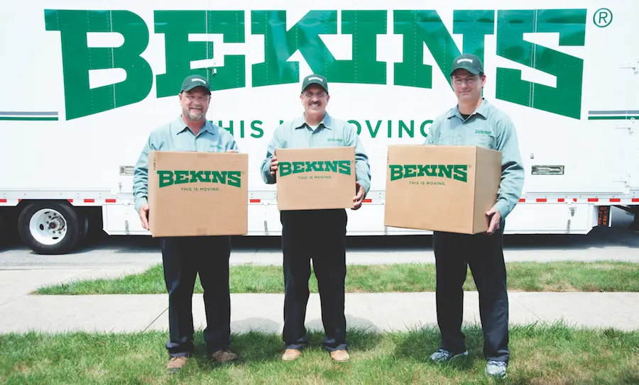 Three Bekins Employees holding Bekins branded cardboard boxes in front of a Bekins Moving Truck