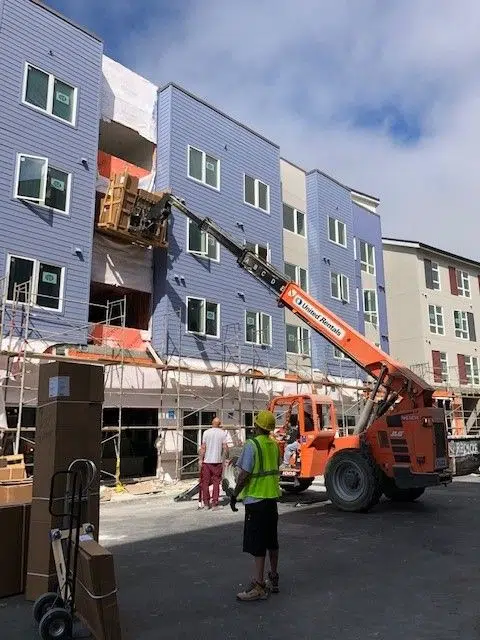 Workers unloading large boxes off a scissor lift and onto a building's balcony.