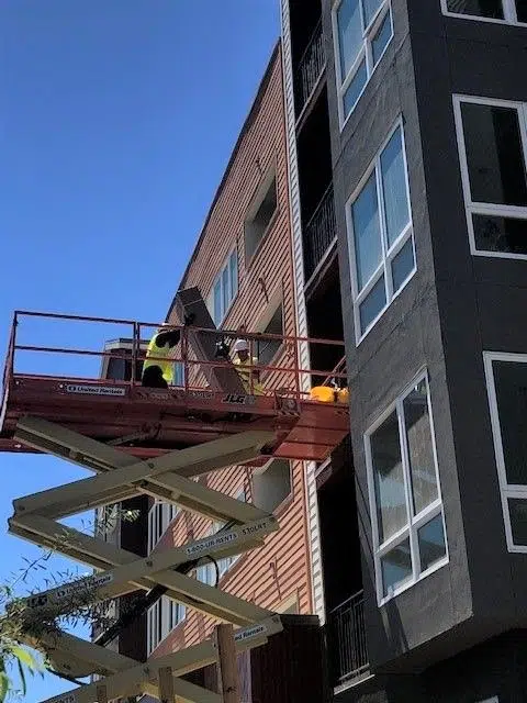 Two workers unloading large boxes off a scissor lift and onto a building's balcony.