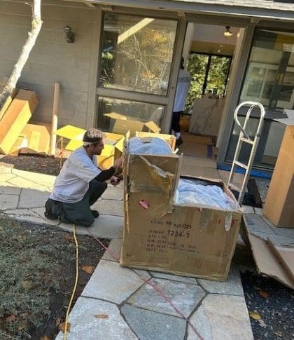 A worker carefully unpacks a furniture item in front of a residential home.