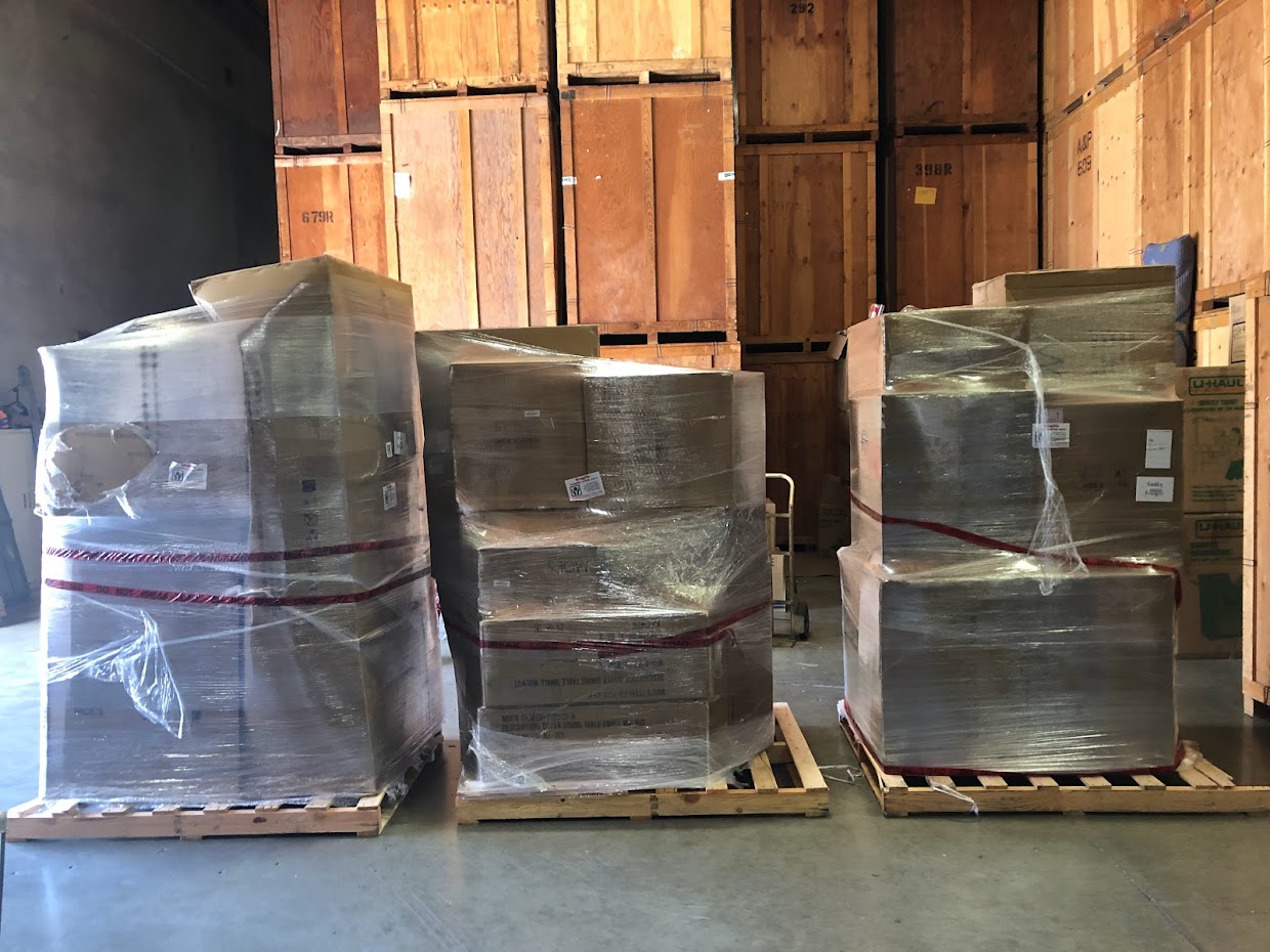 Tightly-wrapped boxes sit on three pallets in a clean warehouse.
