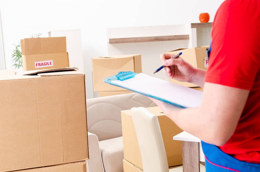 A person is holding a clipboard and checking items off a list while looking over an office filled with packed boxes and furniture.